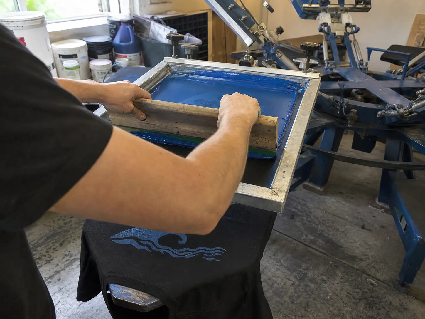 Printer pulling blue ink through a screen on a manual press